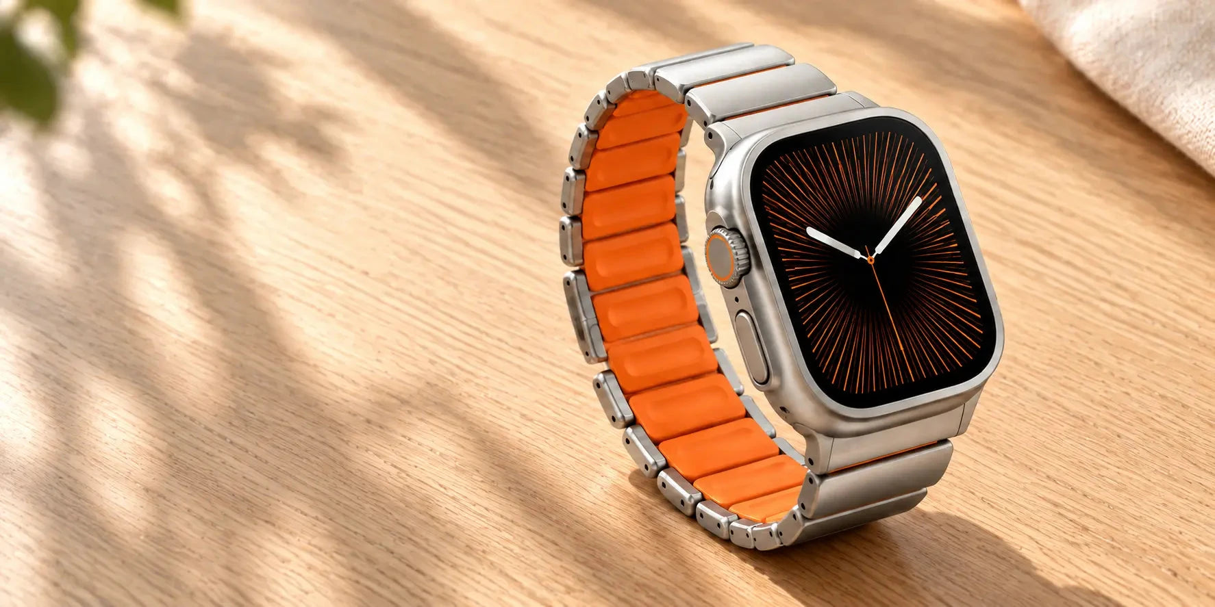 Silver smartwatch band with orange inner links resting on a wooden surface.